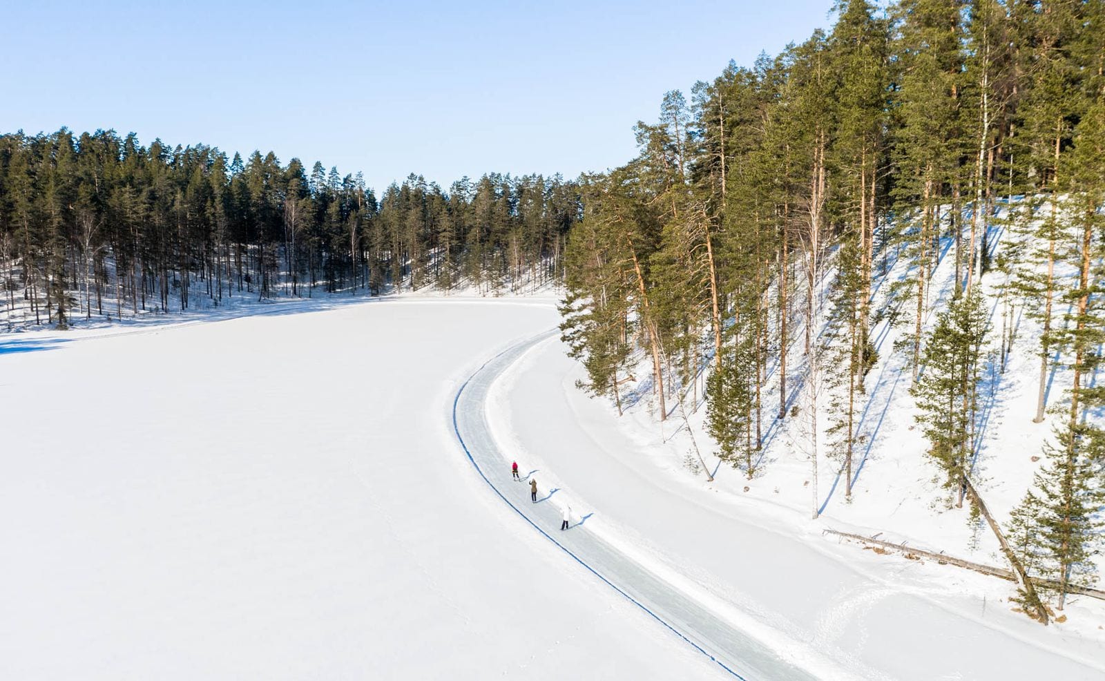 Geveegde schaatsbaan die langs de beboste oever van het Saimaameer buigt, met twee schaatsers