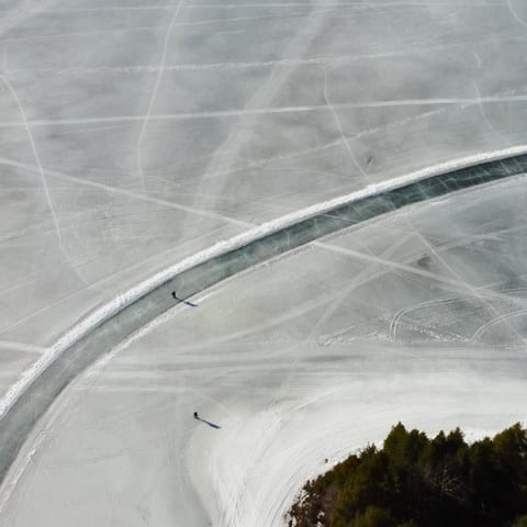 Luchtfoto van een geveegde schaatsbaan die in een bocht over een besneeuwd meer loopt