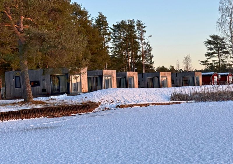 Houten huisjes in de winter aan een besneeuwd, bevroren meer, in het lage avondlicht