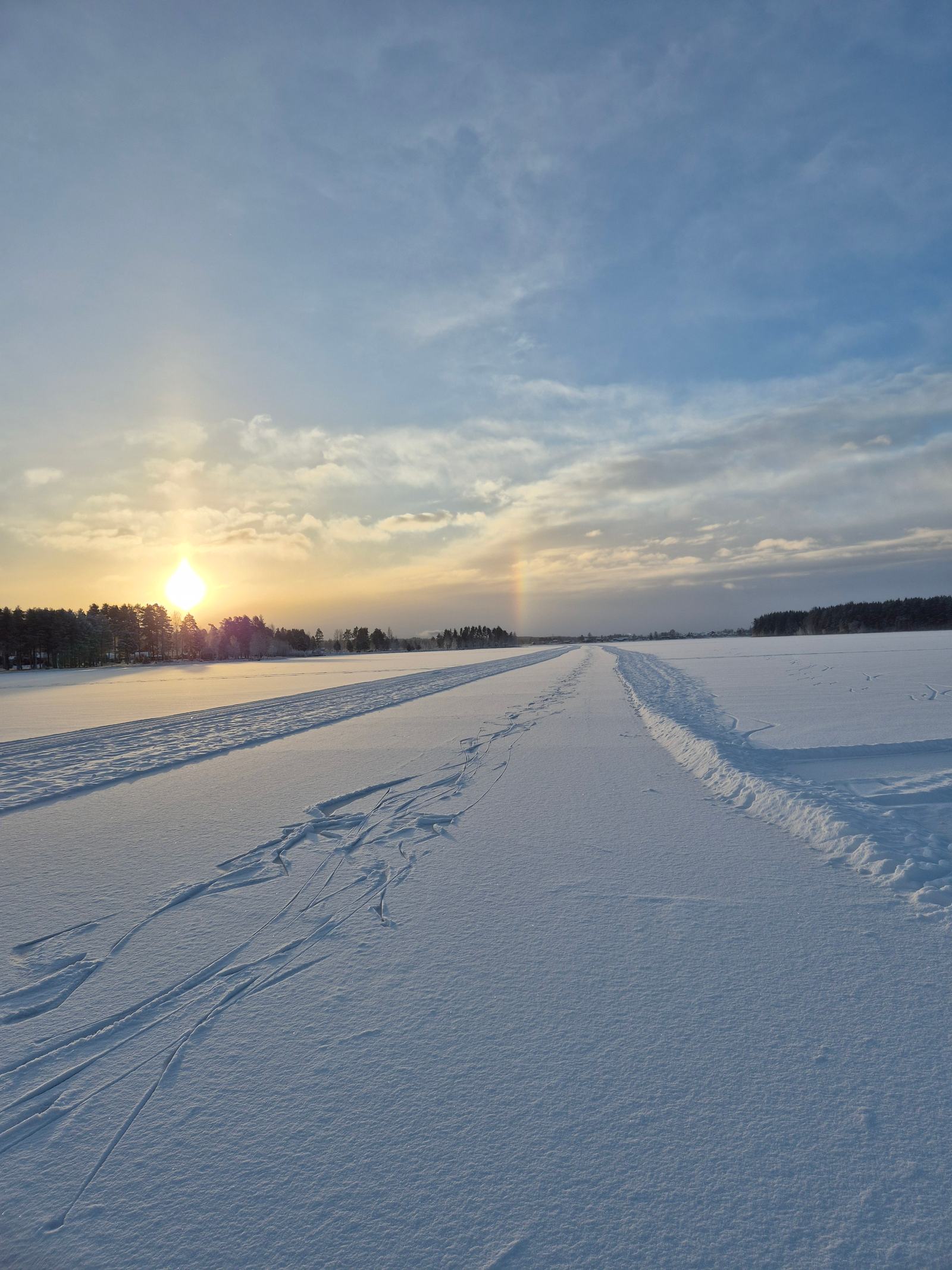 Lange geveegde schaatsbaan over natuurijs richting de horizon, met laagstaande zon