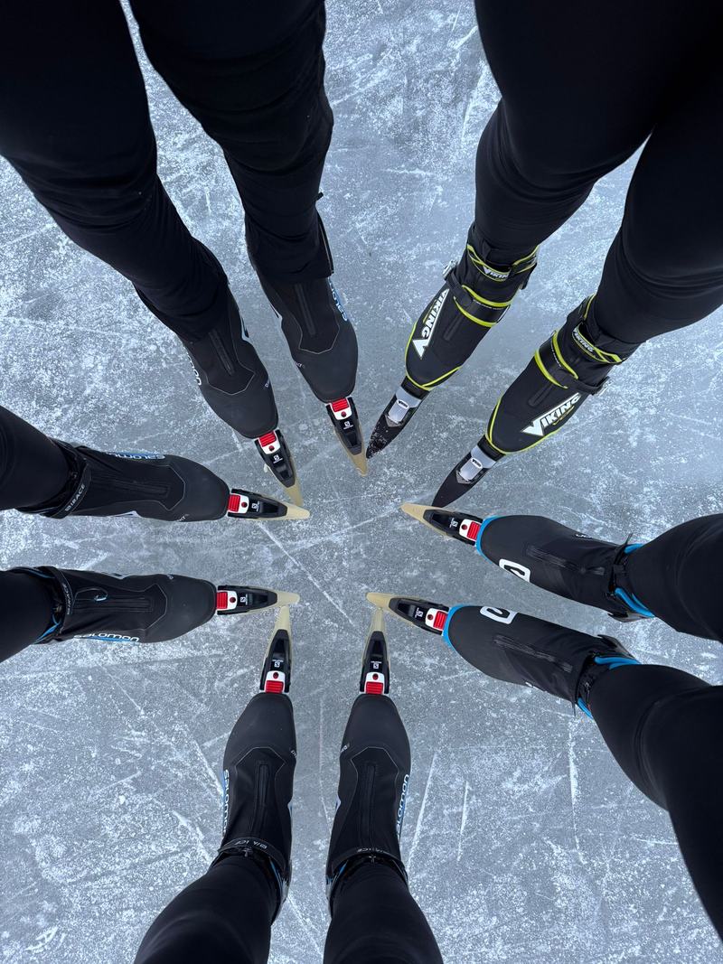 Van bovenaf gezien: de schaatsen van een groep staan in een cirkel met de punten naar elkaar toe op bekrast ijs